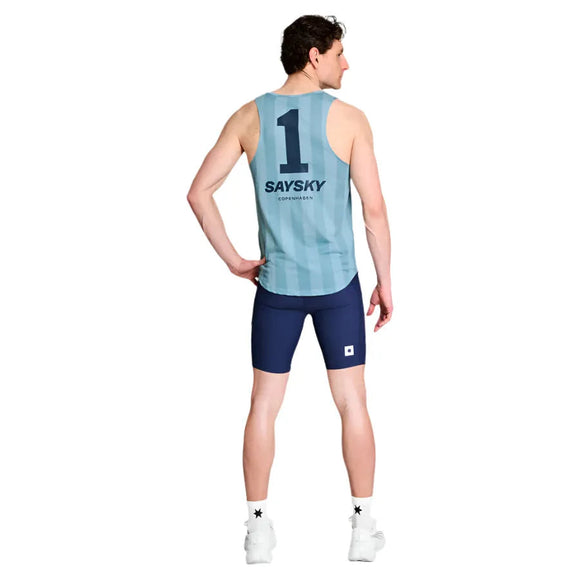 En mand kigger væk, iført en lyseblå Stripe Combat Singlet, Herre, Blue Aop fra Saysky med "1" og "SAYSKY Copenhagen" på ryggen, sammen med marineblå shorts, hvide sokker og hvide sportssko.