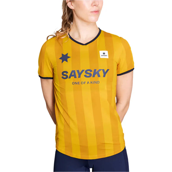 En kvinde er iført Saysky W Stripe Combat T-Shirt, Dame, Yellow Aop - med gule striber, sort kant, en stjerne, teksten ONE OF A KIND og Saysky-logoet - der vender lidt til siden. Ideel til sportstøj til kvinder.