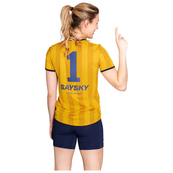 En kvinde står med ryggen til og er iført den gule W Stripe Combat T-shirt fra Saysky med "1" på ryggen. Hun peger opad med sin højre pegefinger og har håret bundet tilbage.
