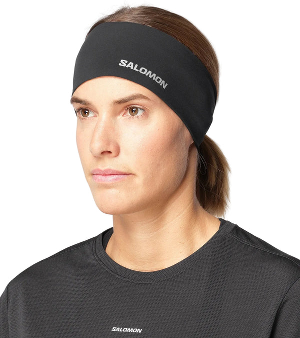 En person bærer et sort Salomon Sense Aero-pandebånd, unisex, i farven Deep Black, med et logo på siden.