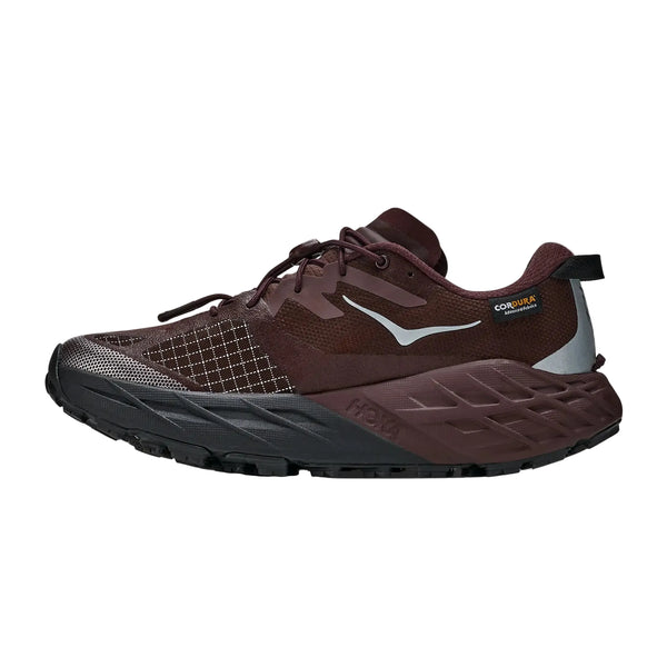 Hoka Speedgoat 7 GTX til kvinder er en atletisk løbesko i farverne Deep Mauve og sort, vist i profil mod en ensfarvet hvid baggrund. Med sorte og hvide detaljer, en tyk sål, mesh-materiale ved tåen og et Cordura-mærke nær hælen er denne trailsko designet til at holde til alle typer terræn. Vejrbestandige GORE-TEX-elementer hjælper med at holde dine fødder tørre.