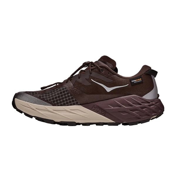 Speedgoat 7 GTX er en trailsko til mænd fra Hoka i farverne Spiced Chocolate og River Rock Grey. Den har sorte snørebånd, en tyk sål med geometriske mønstre på mellemsålen, slidstærkt mesh og detaljer i ruskind samt et diskret GORE-TEX-mærke ved hælen. Dens strukturerede mønster er designet til ujævnt terræn – et ikonisk træk ved Speedgoat-serien.