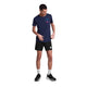 En mand i en marineblå Statement Flow T-shirt til mænd fra Saysky, sorte shorts, hvide sokker og sorte sportssko står på en hvid baggrund, mens han kigger ned og retter på sin skjorte.