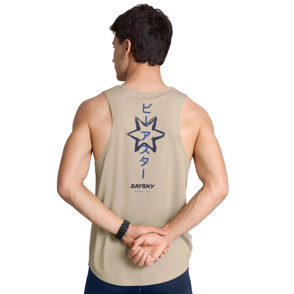 En mand iført en Saysky Statement Combat Pro Singlet, Herre, Sand står med ryggen til kameraet og hænderne foldet bag ryggen. Hans hurtigtørrende singlet har et stort stjernemotiv og japanske tegn trykt på ryggen og tilbyder fremragende åndbarhed. Han bærer et sort ur på venstre håndled.