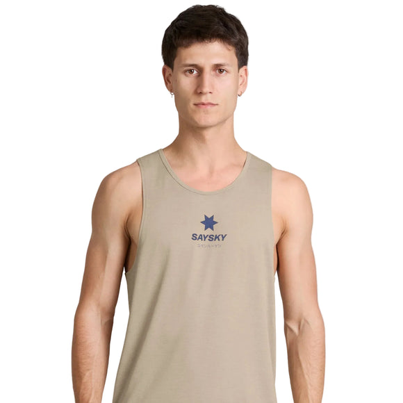 En mand med kort brunt hår har en Saysky Statement Combat Pro Singlet, Herre, Sand på, som er beige med SAYSKY-logoet og en blå stjerne på forsiden. Han står med ansigtet vendt mod kameraet foran en ensfarvet hvid baggrund med et neutralt udtryk. Singletten er kendt for sit hurtigtørrende materiale og fremragende åndbarhed, hvilket sikrer komfort under intens aktivitet.