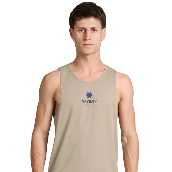En mand med kort brunt hår har en Saysky Statement Combat Pro Singlet, Herre, Sand på, som er beige med SAYSKY-logoet og en blå stjerne på forsiden. Han står med ansigtet vendt mod kameraet foran en ensfarvet hvid baggrund med et neutralt udtryk. Singletten er kendt for sit hurtigtørrende materiale og fremragende åndbarhed, hvilket sikrer komfort under intens aktivitet.