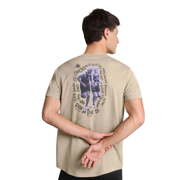 En mand står med ryggen til kameraet, hænderne foldet bag ryggen, iført en sandfarvet Saysky Statement Combat Pro T-shirt med et motiv af to løbere og en cirkulær tekst med løberelaterede sætninger som f.eks. »Run or Die«.