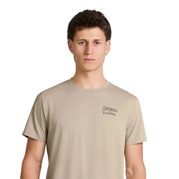 En person med kort, mørkt hår har en sandfarvet Statement Combat Pro T-shirt fra Saysky på, med teksten »SAYSKY RUNNING« på venstre bryst. Den ensfarvede hvide baggrund fremhæver personen, der ser fremad med et neutralt udtryk.