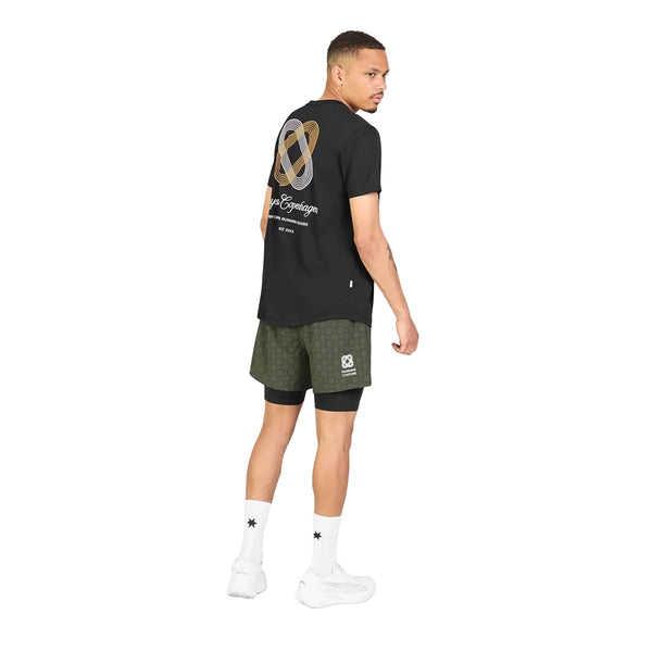 En mand iført en sort Statement Combat Pro-T-shirt med et motiv på ryggen, olivengrønne sportsshorts med sorte leggings under, hvide sokker og hvide sneakers.