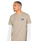 En mand iført Saysky Statement Combat Pro T-shirt, Herre, Sand – en beige kortærmet T-shirt med et lille marineblåt mærke – over en hvid langærmet trøje, står foran en ensfarvet hvid baggrund og kigger mod venstre. Denne hurtigtørrende løbetrøje til mænd fra Saysky kombinerer både komfort og stil til enhver aktiv dag.
