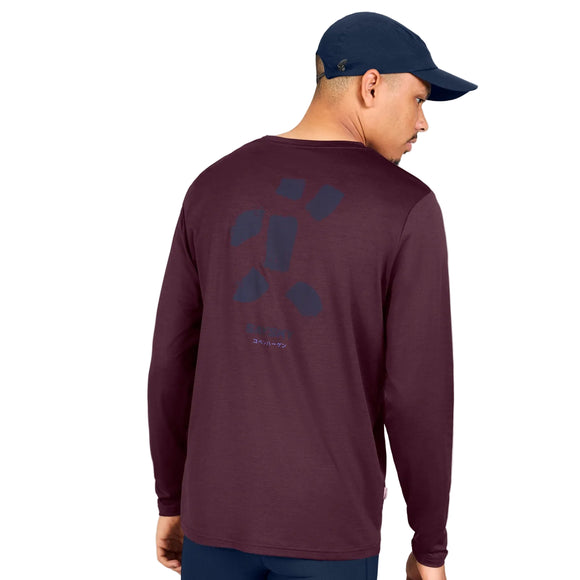 En mand iført en marineblå kasket og en langærmet »Statement Pace Long Sleeve, Herre, Burgundy« fra Saysky står med ryggen til. Bagsiden af den hurtigtørrende trøje er prydet med et enkelt, abstrakt mønster og en lille tekst. Baggrunden er hvid.