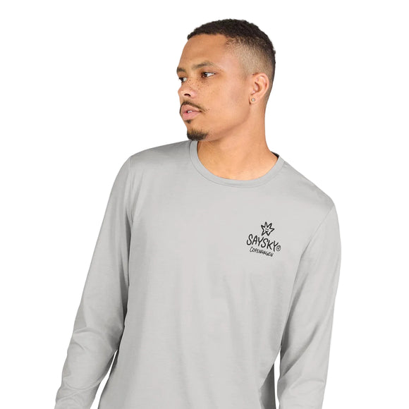 En mand med kort hår og et velplejet skæg har en Saysky Statement Pace Long Sleeve, Herre, Grå, på, med et SAYSKY Copenhagen-logo på venstre bryst. Han kigger til venstre foran en ensfarvet lys baggrund. Det hurtigtørrende materiale sikrer optimal komfort under hver eneste løbetur.