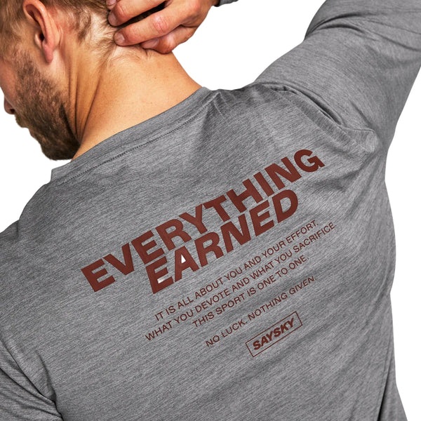En person iført Statement Pace Long Sleeve, Herre, Grey fra Saysky – en grå, åndbar træningstrøje med den markante røde tekst »EVERYTHING EARNED« og mindre motiverende citater om indsats, opofrelse og sport – samt Saysky-logoet trykt på ryggen.