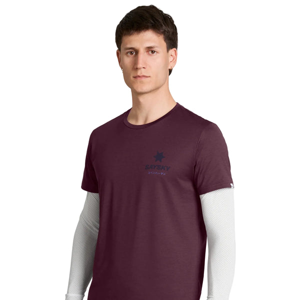 En person med kort, brunt hår bærer en Saysky Statement Pace T-shirt, Herre, i farven burgundy – i herremodel – med korte ærmer, der er lagt over en hvid langærmet skjorte, og står foran en ensfarvet hvid baggrund. T-shirten er designet til træning og har et lille logo og en tekst på venstre bryst.