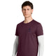 En person med kort, brunt hår bærer en Saysky Statement Pace T-shirt, Herre, i farven burgundy – i herremodel – med korte ærmer, der er lagt over en hvid langærmet skjorte, og står foran en ensfarvet hvid baggrund. T-shirten er designet til træning og har et lille logo og en tekst på venstre bryst.