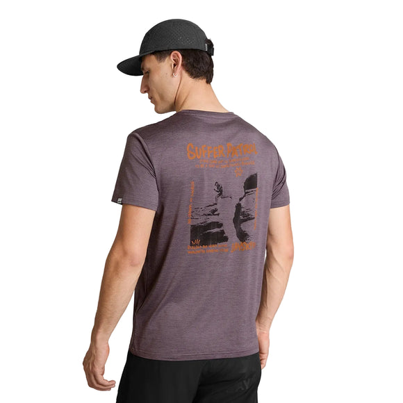 En mand iført en mørkegrå kasket og en Saysky Statement Pace T-shirt, Herre, Lilla, står med ryggen til, så det orange tryk på ryggen kommer til sin ret. Han står foran en ensfarvet hvid baggrund, klar til træning eller fritidstøj.