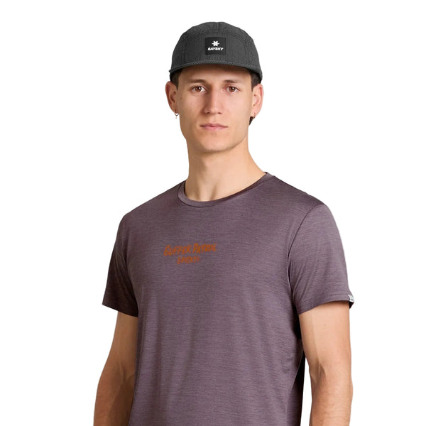 En person står foran en hvid baggrund iført en mørk baseballkasket og en Saysky Statement Pace T-shirt, Herre, lilla, med lille orange tekst på brystet. Personen kigger direkte ind i kameraet med et neutralt udtryk og udstråler en afdæmpet træningsstemning.