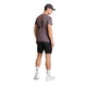 En mand står med ryggen til og har en grå kasket på, en lilla Saysky Statement Pace T-shirt til mænd med et grafisk motiv, sorte shorts, hvide sokker med sorte stjerner og hvide sneakers. Dette trendy herre-træningslook fremstår på en ensfarvet hvid baggrund.