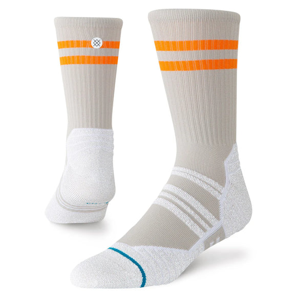 Et par beige Static Gripper Splatter Crew-løbesokker fra Stance, unisex i lysegrå, med to vandrette orange striber nær toppen og hvide, polstrede såler. Disse sportsstrømper har yderligere hvide og grå accentlinjer, et lille cirkulært logo på siden samt skridsikre grippaneler, der giver øget stabilitet under bevægelse.