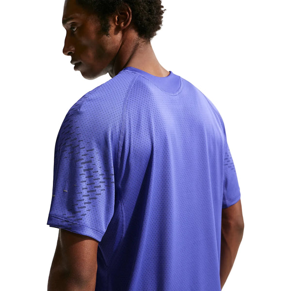 En person iført en lilla Nike Stride Plus SS Running Top, Herre (Lapis/Deep Royal Blue/Reflective Silver), med perforeret Dri-FIT-stof, vender ansigtet væk og ser til venstre mod en almindelig hvid baggrund.