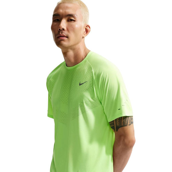 En person med kort blondt hår er iført en neongrøn Nike Stride SS Running Top, Herre, Volt Ice/Reflective Silv, og kigger ind i kameraet med et neutralt udtryk. Baggrunden er helt hvid.