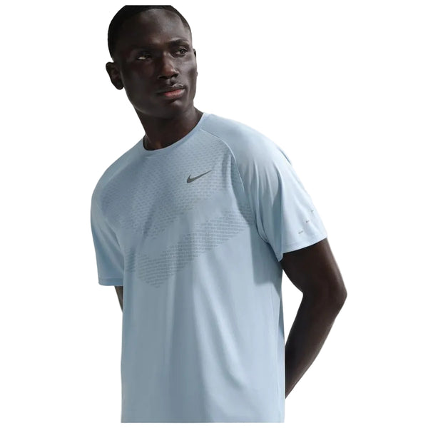 En mand i en Nike Stride SS løbetop til herrer i Lt Armory Blue/Reflective Silver står og kigger lidt til siden mod en almindelig hvid baggrund.