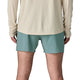 En person vender ansigtet væk fra kameraet iført en langærmet beige skjorte og Patagonia Strider Pro Shorts 5in, Herre i Blue Sage. Kun den nederste del af ryggen, hofterne og benene er synlige på en hvid baggrund.