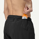 En person placerer en orange sportsernæringsgel i den bagerste lynlåslomme på sorte Patagonia Strider Pro Shorts 7", Herre. Billedet er vist fra taljen og ned og fremhæver disse shorts' praktiske design til aktiv brug.