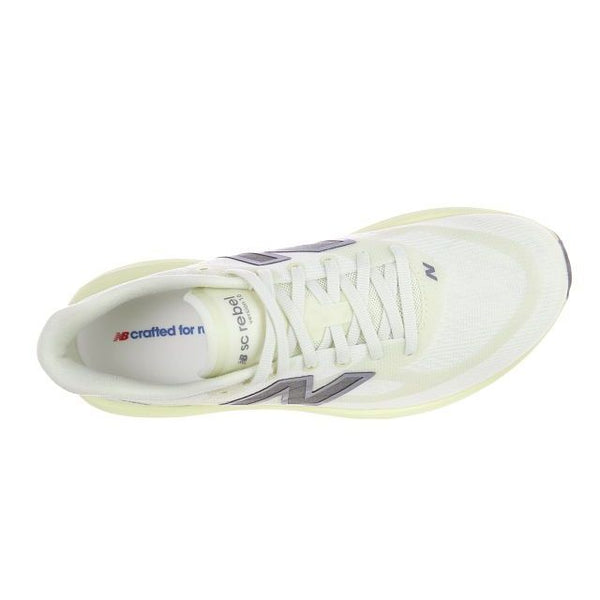 Set ovenfra fremstår New Balance Supercomp Rebel V1, Dame i farven Pistachio Butter som en hvid sportssko med grå detaljer, synlige snørebånd, tunge og det karakteristiske N-logo; indersålen er forsynet med teksten »crafted for« i rødt og blåt. Denne løbesko er en responsiv træningssko designet af New Balance med henblik på optimal komfort og ydeevne.