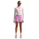En person iført en lyserød langærmet crop top, Nike Swift Df Mr 2in1 Shorts til kvinder i Lt Magenta/Lt Magenta/Reflective Silv, lyse sokker, sneakers og solbriller står med front mod en hvid baggrund.
