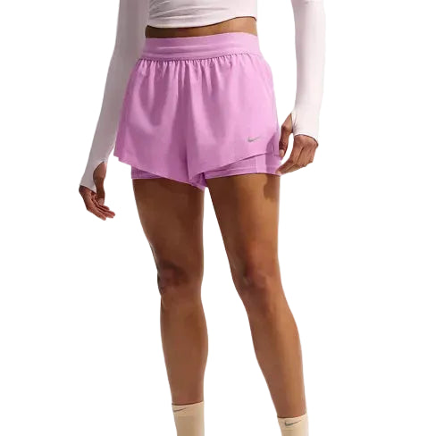 En person i hvid langærmet top og lyslilla Nike Swift Df Mr 2in1 Shorts, Dame (Lt Magenta/Lt Magenta/Reflective Silver), står med afslappede arme; shortsene har et lille Nike-logo på venstre ben.