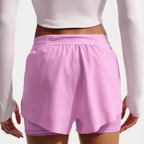 En person iført en langærmet hvid crop top og Nike Swift Df Mr 2in1 Shorts, Dame, Lt Magenta/Lt Magenta/Reflective Silv ses bagfra, stående med armene afslappet ned langs siden.