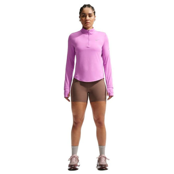 En person står og kigger fremad iført en langærmet Nike Swift UV Half Zip Running Top til kvinder i Lt Magenta/Reflective Silver, sammen med brune cykelshorts, grå sokker og lilla sportssko på en hvid baggrund.