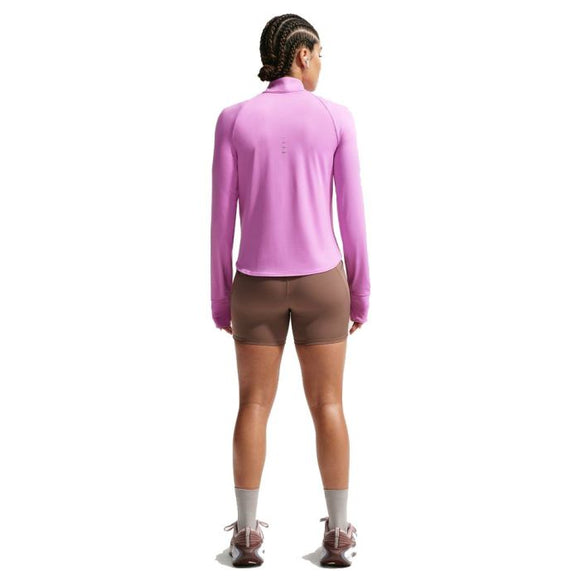 En person med flettet hår kigger væk og er iført en Nike Swift UV Half Zip Running Top til kvinder i Lt Magenta/Reflective Silver, brune shorts, grå sokker og brune sportssko på en hvid baggrund.