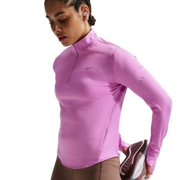 En kvinde i Nike Swift UV Half Zip Running Top, Dame, Lt Magenta/Reflective Silv og brune leggings strækker benet, mens hun lytter til musik med trådløse øretelefoner.