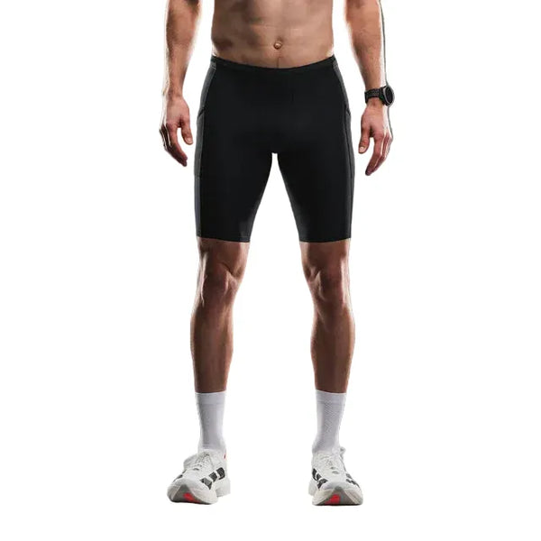 En mand bærer Fusion TEMPO! Run Tights i sort unisex, stylet med hvide sokker, hvide sneakers og et armbåndsur. Billedet (skuldre til fødder) på en almindelig hvid baggrund fremhæver det slanke design af disse tights.