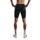 En person står med ryggen til på en hvid baggrund iført Fusion TEMPO! Run Tights (unisex, sort) sammen med et mørkt armbånd, hvide sokker med tekst og hvide sneakers med sorte striber og orange detaljer.