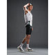 En mand i sportstøj står på en grå baggrund iført en hvid og grå tanktop, Fusion TEMPO! Run Tights (Unisex, Black), hvide sokker og hvide løbesko, mens han løfter solbrillerne af hovedet med den ene hånd.