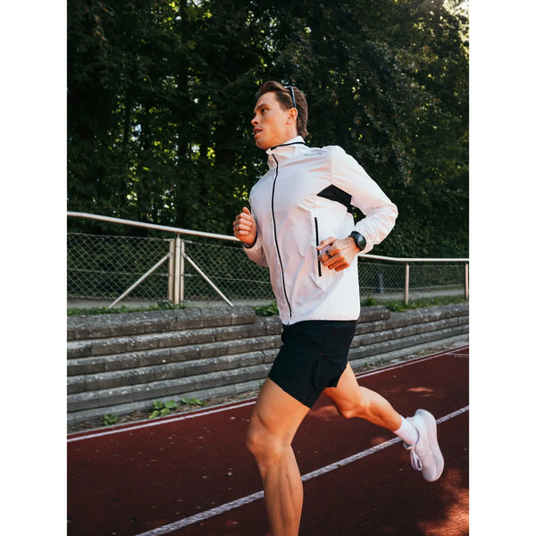 En mand iført en hvid Fusion Tempo! Two Run-jakke (herre) og sorte shorts løber på en løbebane.