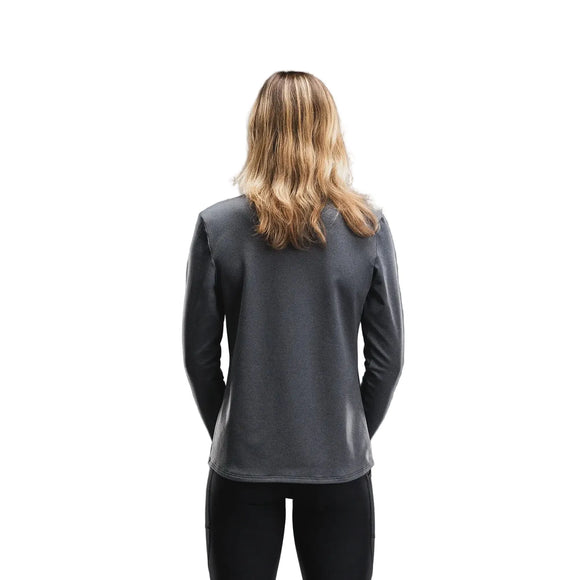 En person med skulderlangt, bølget blondt hår står med ryggen til kameraet iført en Fusion Tempo! Shield Zip, Dame i mørkegrå og sorte bukser foran en hvid baggrund.
