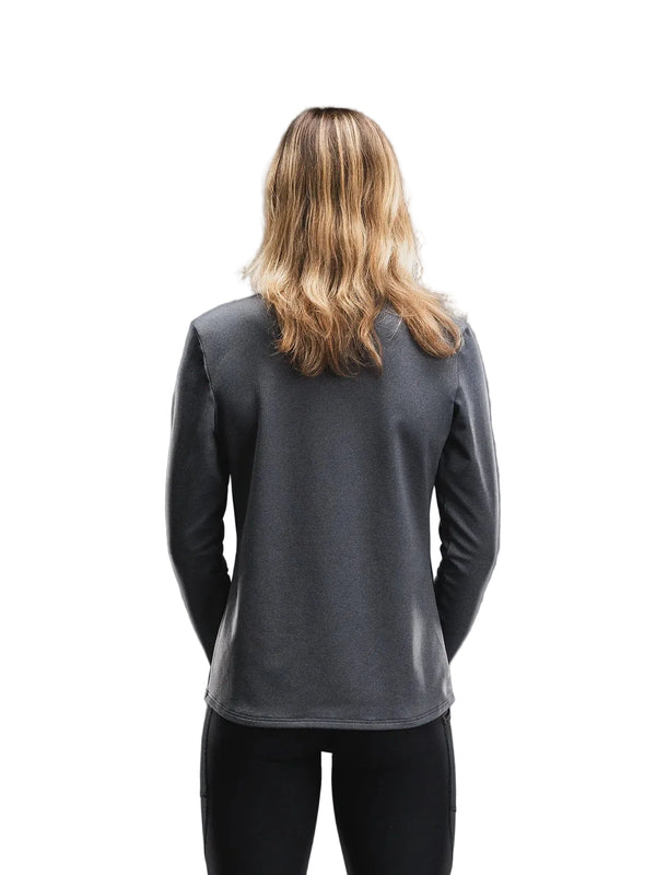 En person med skulderlangt, bølget blondt hår står med ryggen til kameraet iført en Fusion Tempo! Shield Zip, Dame i mørkegrå og sorte bukser foran en hvid baggrund.
