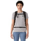 En person med kort, krøllet hår har en grå T-shirt, blå leggings og en sort Patagonia Terravia Pack 14L med bryst- og taljestropper på og står foran en ensfarvet hvid baggrund.