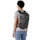En person med kort, krøllet hår har en grå T-shirt og blå leggings på og bærer en sort Patagonia Terravia Pack 14L. Personen står med ryggen til kameraet og viser ryggen på Patagonia-rygsækken samt sit tøj.