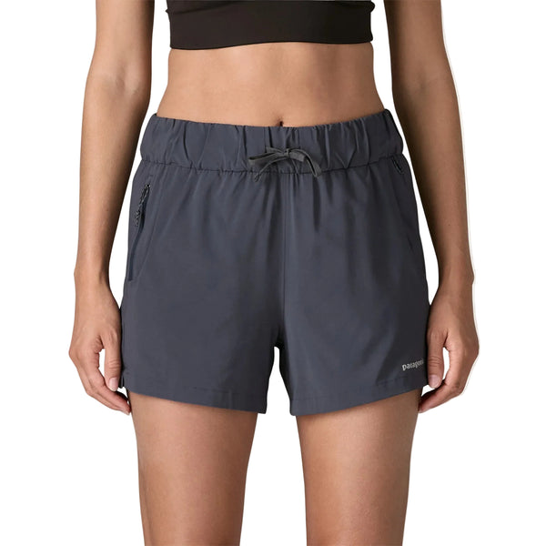 En person iført en sort crop top og Patagonia Terrebonne Shorts, Dame i Smolder Blue med sidelommer med lynlås og Patagonia-logo på nederste venstre ben, står på en almindelig hvid baggrund.