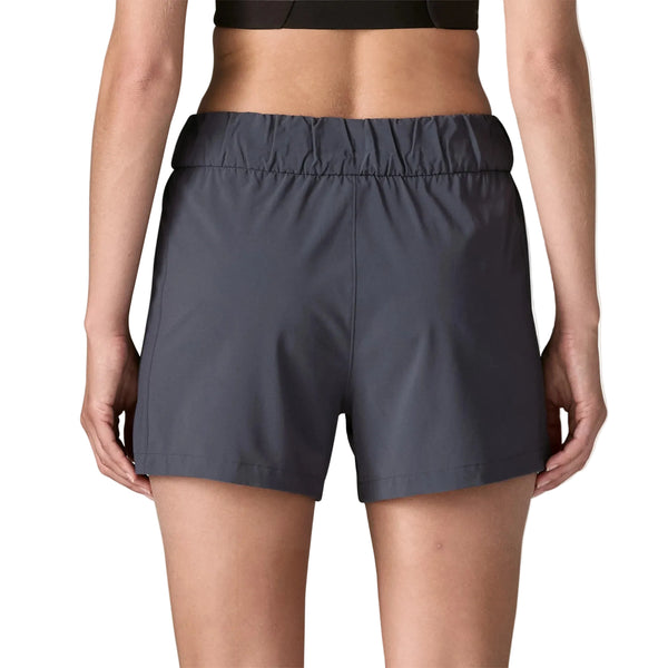 En person vises fra taljen og ned iført Patagonia Terrebonne Shorts, Dame, i Smolder Blue, med en sort sports-bh. Personens ryg vender mod kameraet.