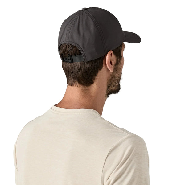 En mand ses bagfra iført en Patagonia Terrebonne Hat, Unisex, Black - en hurtigtørrende kasket af genanvendte materialer - med justerbar rem og en del af håret synligt, samt en lys beige t-shirt på en almindelig hvid baggrund.