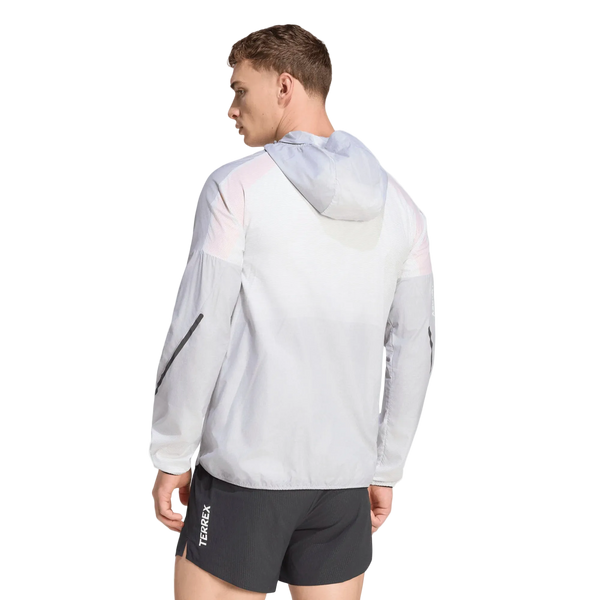 En person iført en Adidas Terrex Xperior Light Windweave-jakke (herre) i farvekombinationen sort/hvid samt sorte sportsshorts står med ryggen til og kigger mod venstre. Den lette vindjakke har en lomme med lynlås på venstre ærme, hvilket gør den ideel til trail-løb. Baggrunden er ensfarvet hvid.