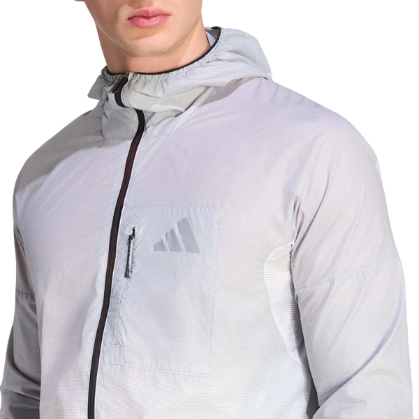 En person iført Adidas Terrex Xperior Light Windweave-jakken, herre, sort/hvid, med sort lynlås og et Adidas-logo på venstre brystlomme. Billedet fokuserer på overkroppen og en del af ansigtet på en hvid baggrund og fremviser denne stilfulde vindjakke, der er designet til trail-løbsentusiaster.