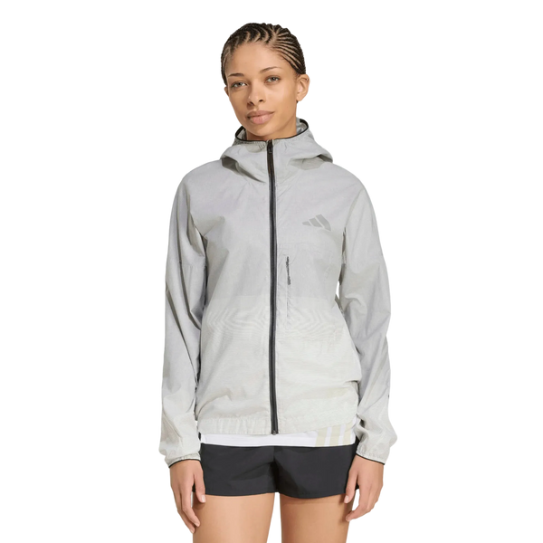 En person med flettet hår har en sort og hvid adidas Terrex Xperior Light Windweave-jakke til kvinder og sorte shorts på og står foran en ensfarvet hvid baggrund.