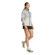 En kvinde iført en Adidas Terrex Xperior Light Windweave-jakke til kvinder i sort og hvidt, kombineret med sorte shorts og hvide løbesko med sorte og neongrønne detaljer, går fremad foran en ensfarvet hvid baggrund.